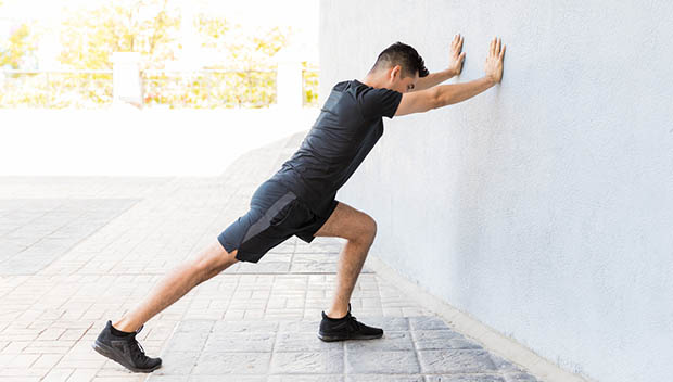 Man leaning on the wall doing calf stretch on his right leg